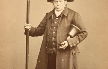 19th century photograph of a man wearing a three-cornered hat, carrying a bell and holding up a long pole