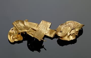 Folded flat peice of gold in the shape of two eagles grasping a fish