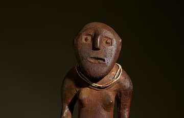 Carved wooden figure in an absract human shape with a beaded necklace and stranded fibre skirt