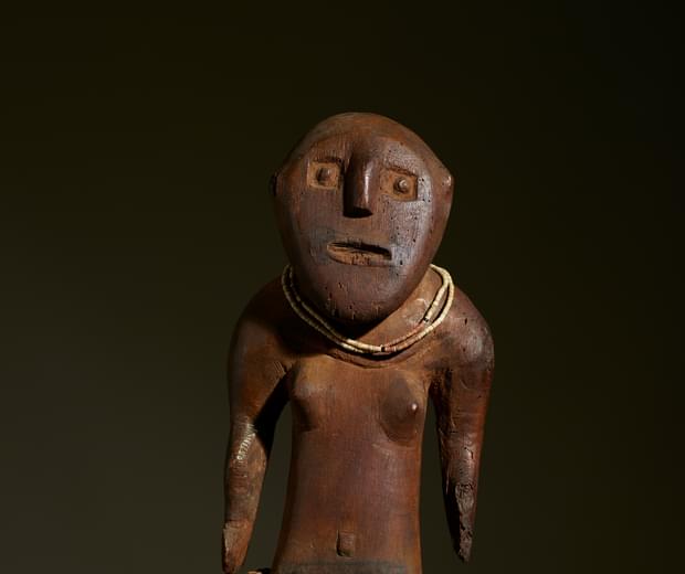 Carved wooden figure in an absract human shape with a beaded necklace and stranded fibre skirt