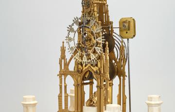 A clock made of delicate gold pieces, in the shape of the framework of a grand building. The cogs, face and handles of the clock are completely exposed