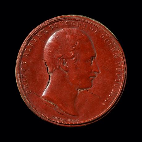 Red coin-type disc, slightly cracked, with the bust of a figure in the centre as he looks to the right