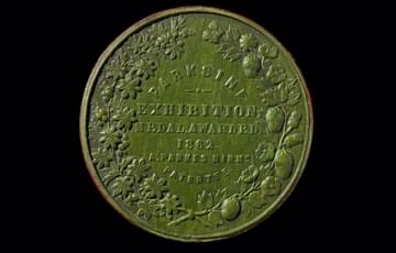 Green coin-type disc with a wreath of fruit, flowers and leaves running around the edge