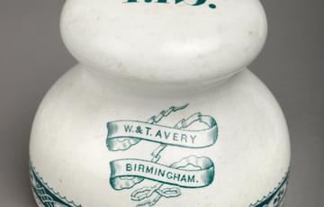 White, door-knob shaped object with green detailing painted at the bottom. 'W&T. Avery Birmingham' is painted in green on its body