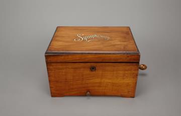 Closed, wooden music box with the word 'Symphonion' painted on the lid in silver, cursive letters