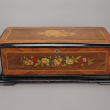 Closed, rectangular music box with flower and instrument painting on the lower lid and a smaller illustration of flowers in the centre of the top lid