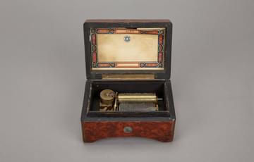 Small open music box with red and blue piping detail on the top box and the metal mechanism sitting in the lower box