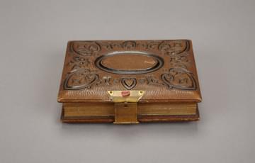 An object that looks like a closed, brown leather diary. It has a black, swirling pattern inscribed on the top