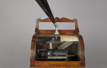 A grained wooden box with a clear domed lid, through which you can see metal mechanisms. From the lid shoots a fluted metal horn