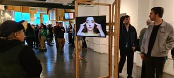 People in a gallery. A woman is staring at a video playing.