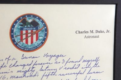 A closeup detail of an Apollo 16 document with logo, "Charles M Juke Astronaut" type in the corner followed by some handwriting.