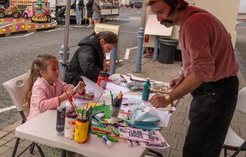 An artist at a table full of art supplies with two children taking part in the craft.