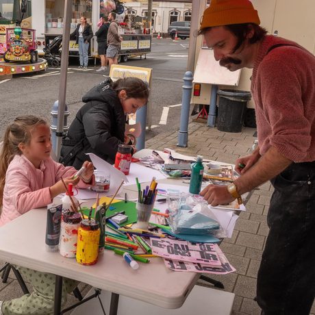 An artist at a table full of art supplies with two children taking part in the craft.