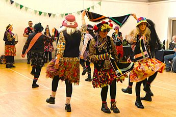 A group of morris dancer in costume dancing in a room.