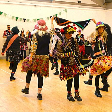 A group of morris dancer in costume dancing in a room.