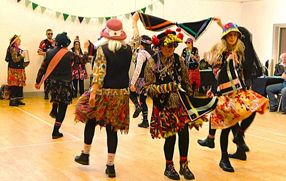A group of morris dancer in costume dancing in a room.