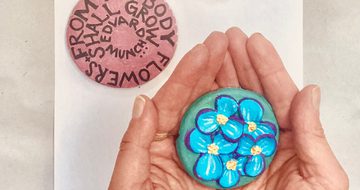 Hands holding a blue flowery clay artwork, with two other artworks on the table.