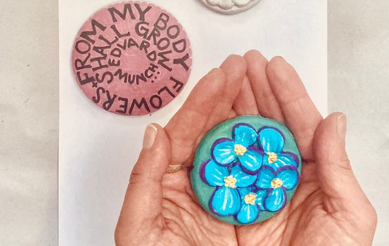 Hands holding a blue flowery clay artwork, with two other artworks on the table.