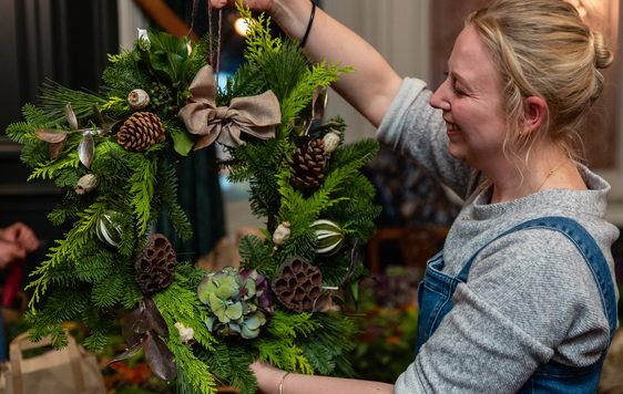 A smiling person holding up a wreath.