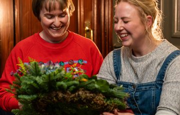 Two people smiling while holding and looking at a wreath.