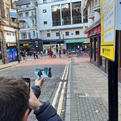 A picture of a man holding a photograph in a street scene