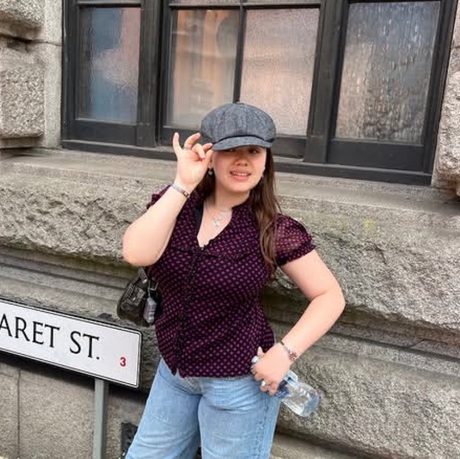 A lady in dark red top wearing a cloth cap next to to a road sign saying Margaret St