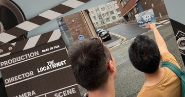 Clapper board which reads 'BMAG on Film the Locationist' alongside a photo of two people on a street holding a photo.
