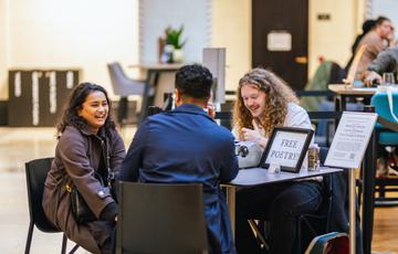 Two people sitting at a desk in front of a man with typewriter and sign that reads Free Poetry!