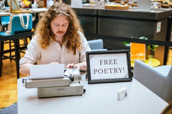 A man sitting at a desk with typewriter and sign that reads Free Poetry!