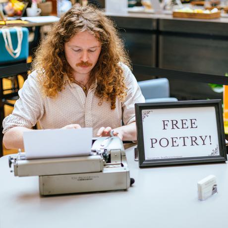 A man sitting at a desk with typewriter and sign that reads Free Poetry!