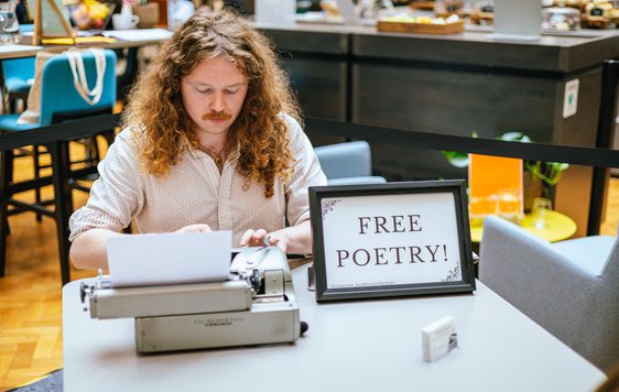 A man sitting at a desk with typewriter and sign that reads Free Poetry!