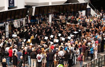 A large crowd watch a group of music performers in New Street train station.