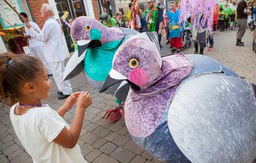 Two people dressed in pigeon costumes interacting with a child.
