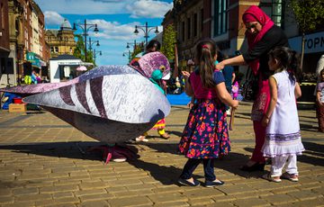 A person dressed in pigeon costumes interacting with a family including and adult and two children on a street.