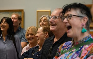 A close up of a group of people in a gallery smiling and laughing.
