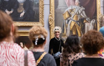 A group of people in a gallery looking at person presenting in front of a painting.
