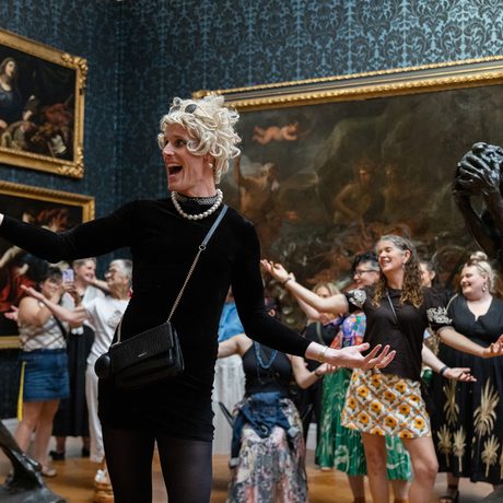 A person performing and holding their arm out, in a gallery setting with people behind copying the movement.