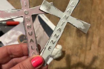 Hand holding one silver and one pink metal cross embossed with names.