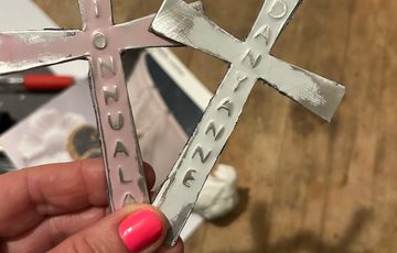 Hand holding one silver and one pink metal cross embossed with names.