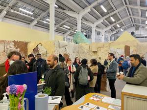 A busy gallery space with a lot of people gathered in small groups chatting.