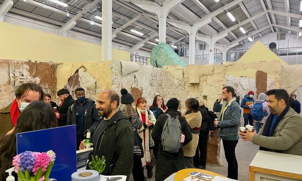 A busy gallery space with a lot of people gathered in small groups chatting.