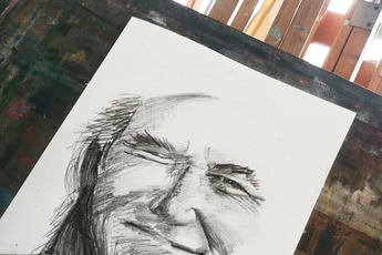 a charcoal sketch of a face on white paper with an art studio in the background of image