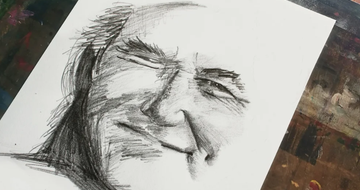 a charcoal sketch of a face on white paper with an art studio in the background of image