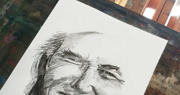 a charcoal sketch of a face on white paper with an art studio in the background of image
