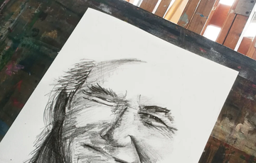 a charcoal sketch of a face on white paper with an art studio in the background of image