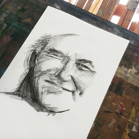 a charcoal sketch of a face on white paper with an art studio in the background of image