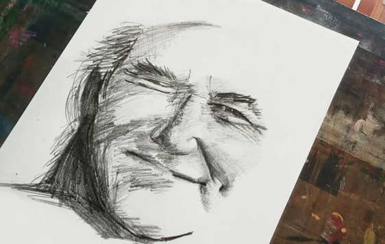 a charcoal sketch of a face on white paper with an art studio in the background of image