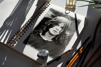 A black and white sketch of Ozzy Osbourne on a spiral notepad with pencils scatted around.