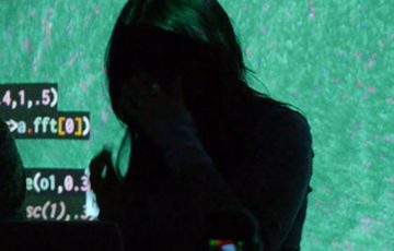 A silhouette of a person with code projected on a screen behind.