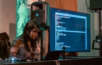 A person perofrming in front of screen and computer.